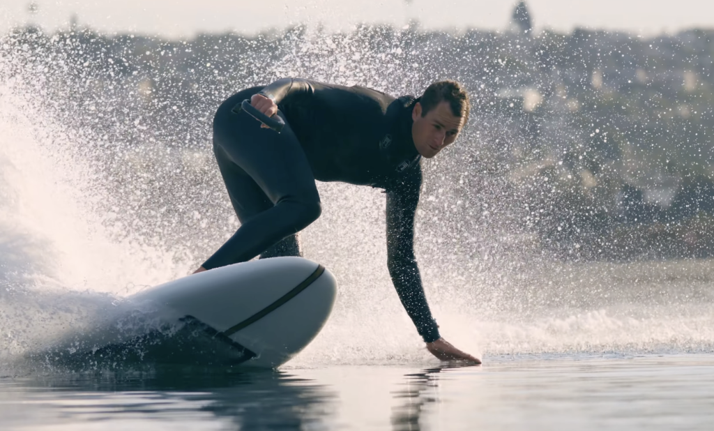Close-up of rider carving a Lind electric surfboard across calm water with spray flying behind