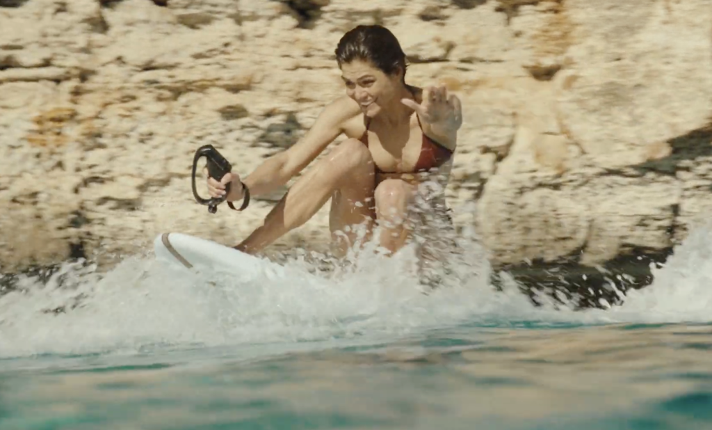 Rider sitting on a Lind electric surfboard while accelerating across shallow water