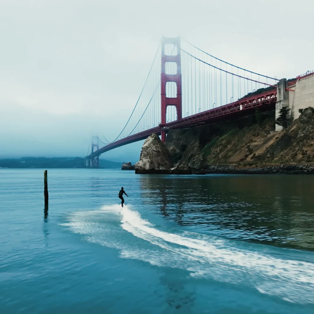 Rider cruising on a Lind electric surfboard across calm water with the Golden Gate Bridge in the background
