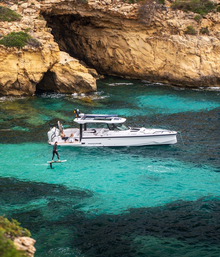 Soft Top eFoil rider cruising beside a boat in clear coastal water, showing family-friendly eFoil use from boat launches and swim platforms.