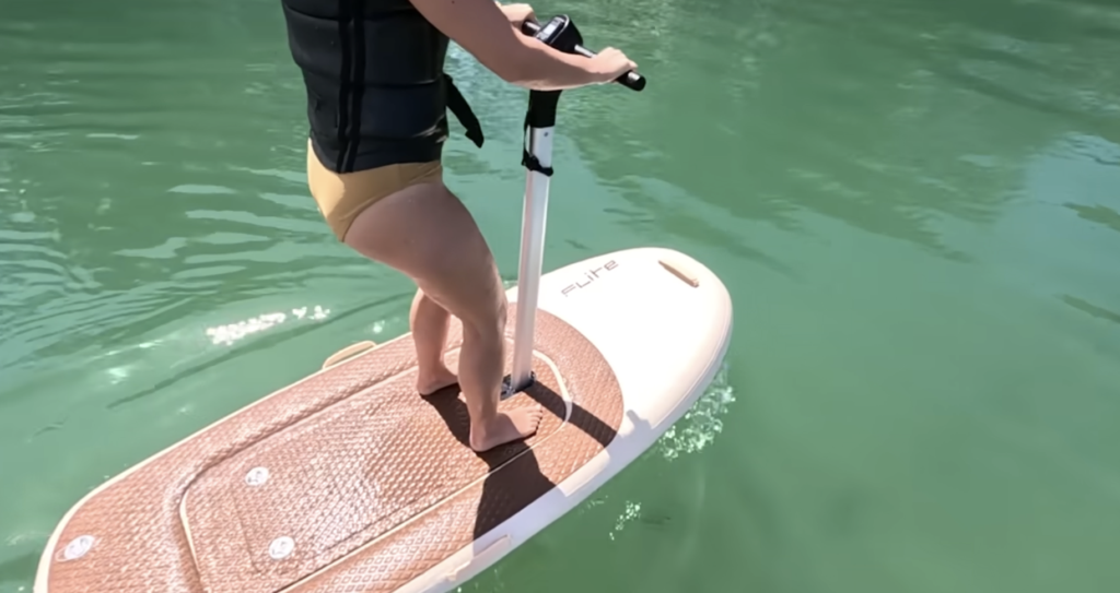 Beginner rider standing on a FliteScooter eFoil with handlebars, demonstrating the stable platform and confidence-building design for first-time eFoilers.